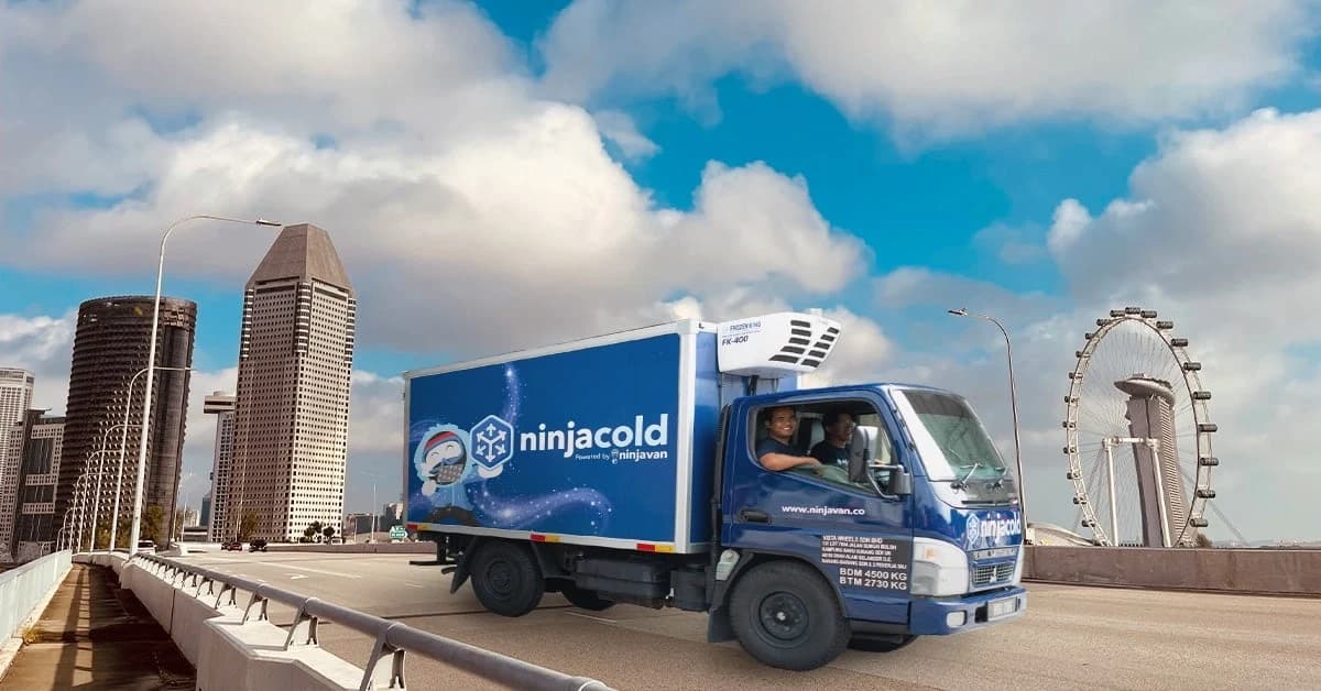 A blue NinjaCold temperature-controlled truck driving along a Singapore waterfront road with the city skyline behind