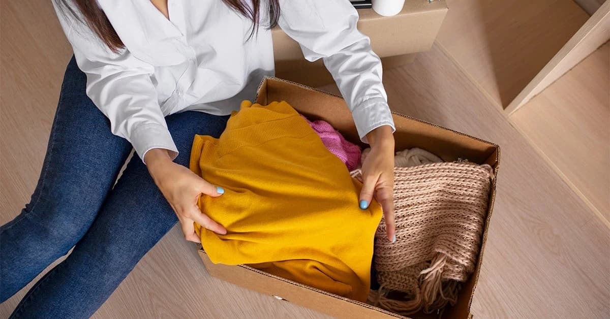 A woman unpacking clothing from a delivery box on the floor
