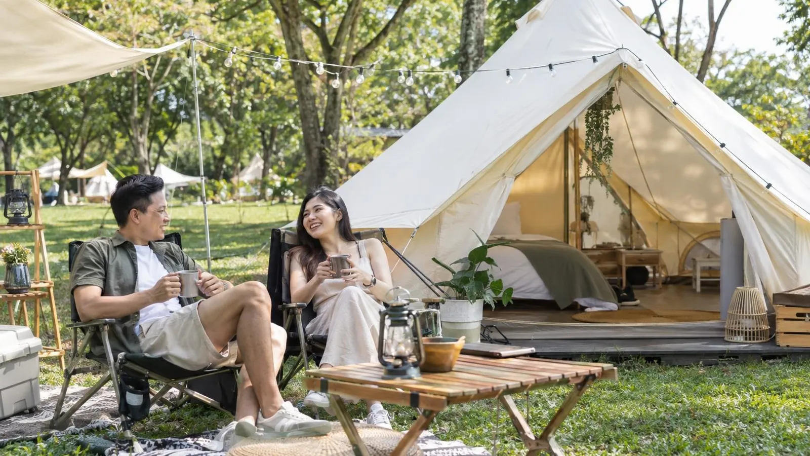 A couple relaxing outside a furnished bell tent at a grassy park campsite