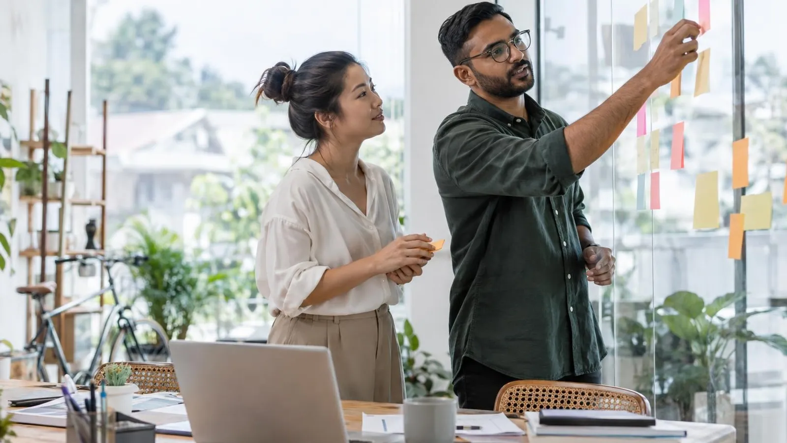A consultant and a small-business owner mapping a workflow with sticky notes on a glass wall in a bright office