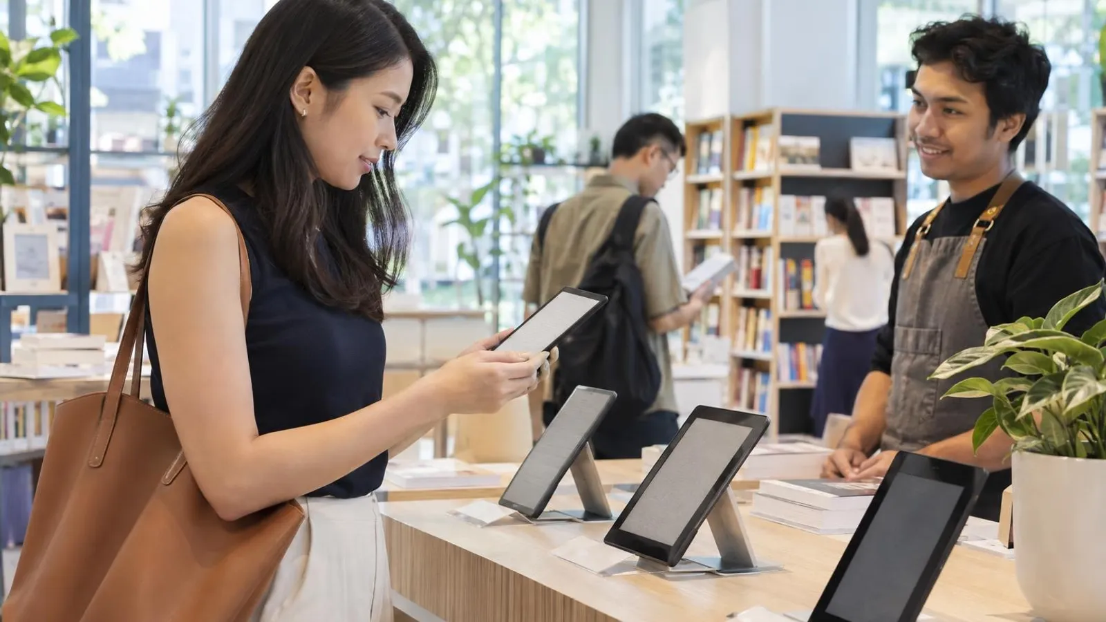 A customer holding an e-reader at a bright counter with several e-readers on display
