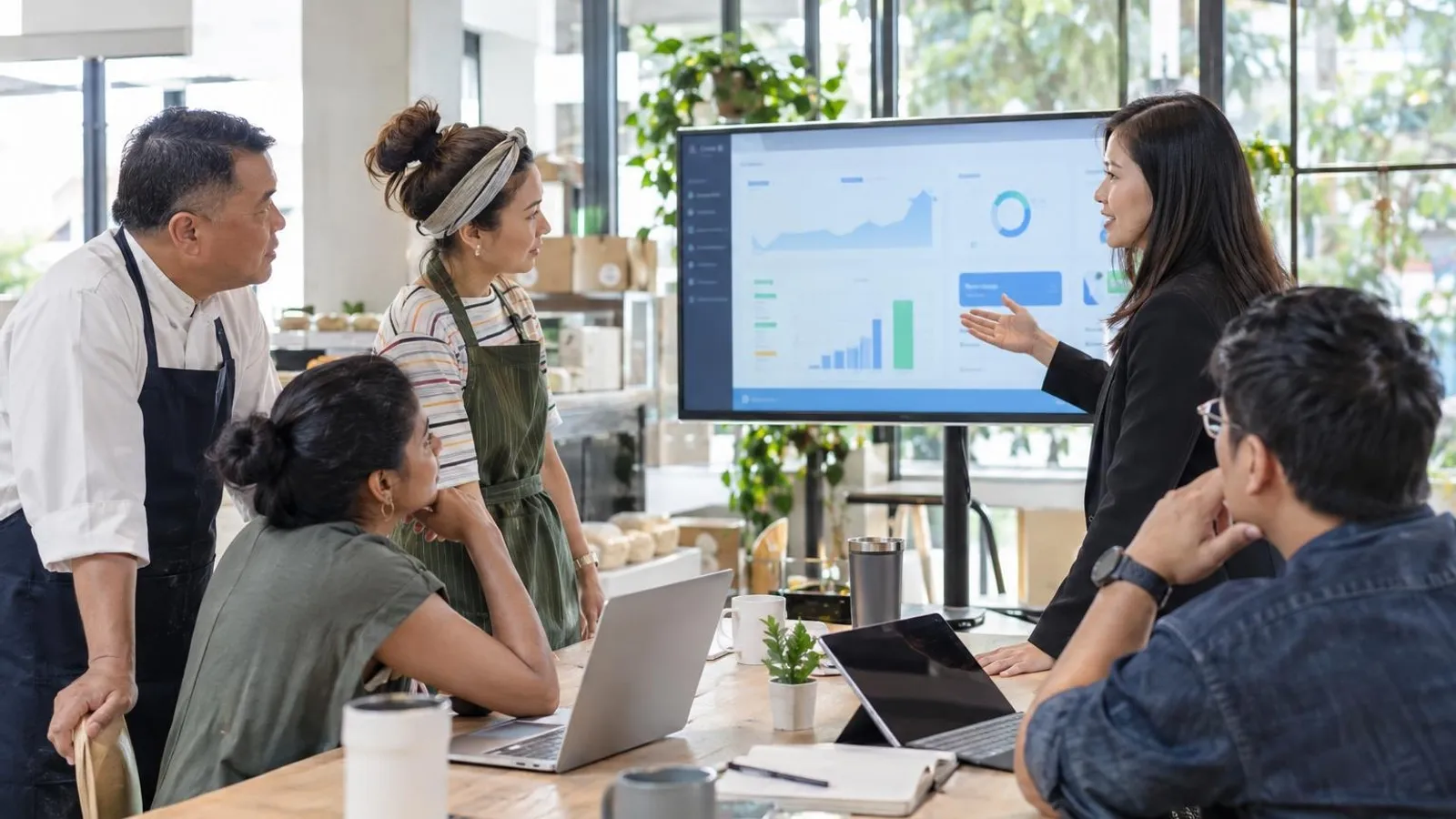 A consultant walking a small-business team through a business software rollout on a large monitor in a bright office