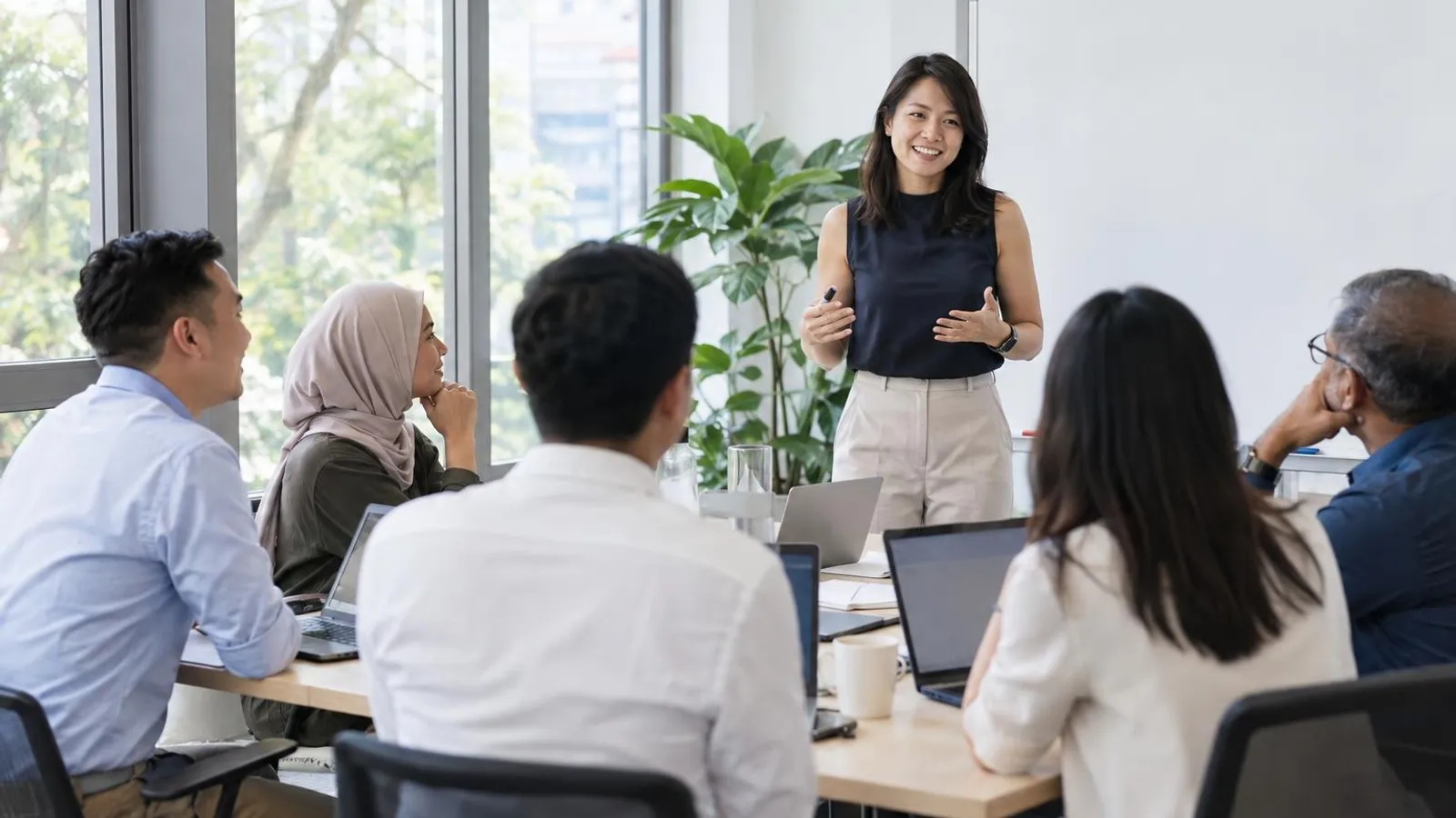 A trainer teaching a small group of office workers around a table with laptops in a bright training room