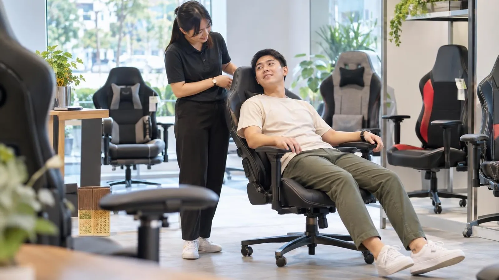 A customer trying out a gaming chair in a bright showroom with several chairs on display