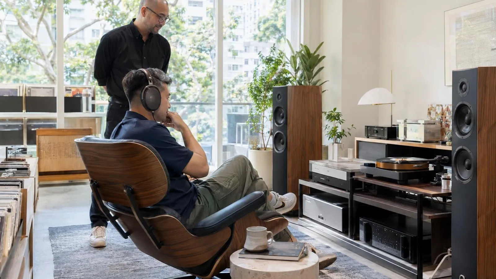 A customer listening through headphones in a calm bright hi-fi listening room with a turntable and tower speakers