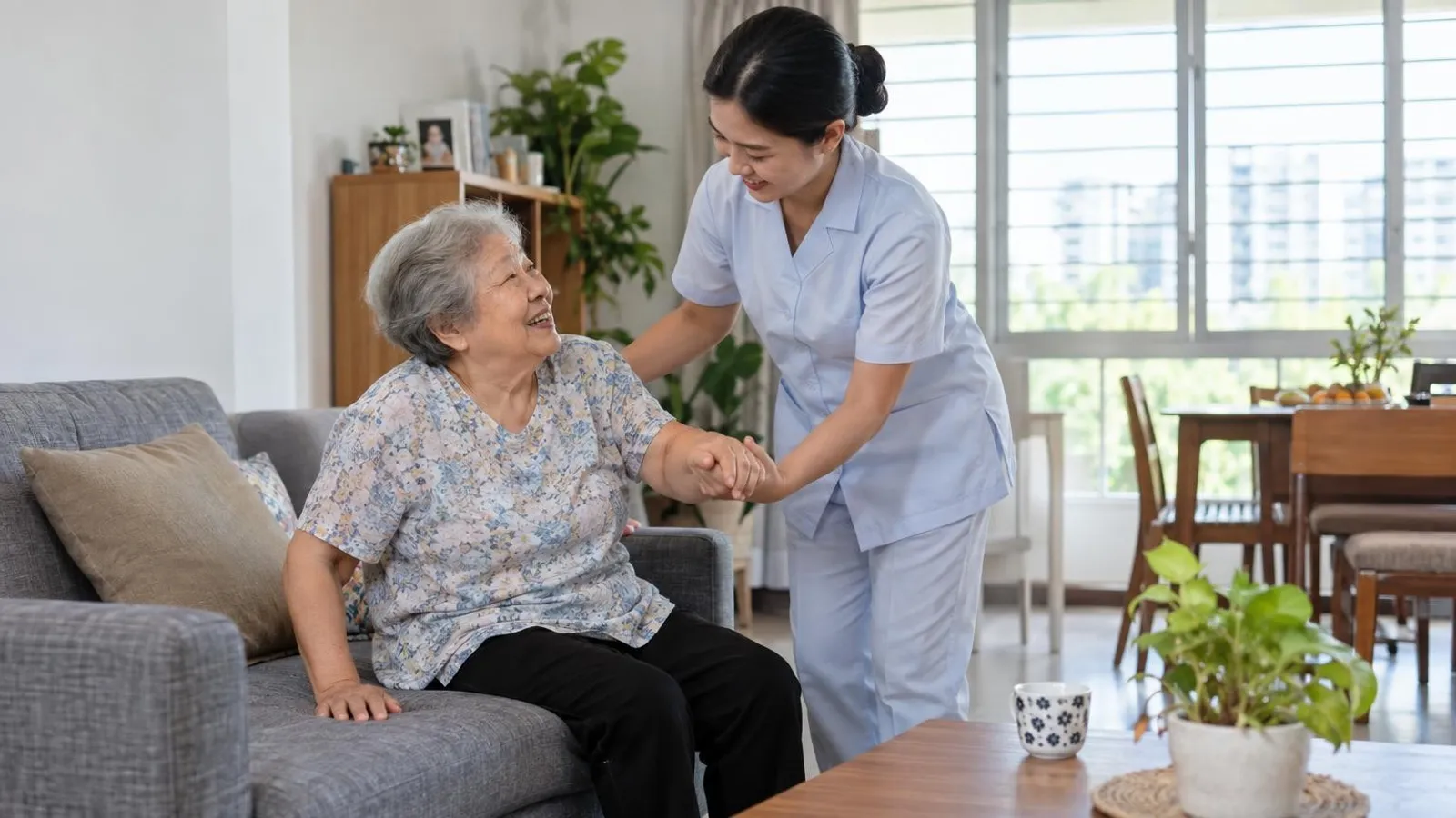 A home-care nurse warmly helping a smiling elderly woman in a bright HDB living room