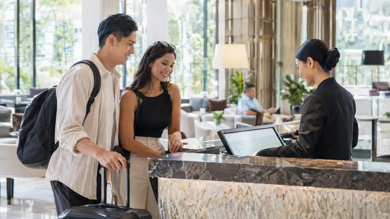 A hotel front-desk staff member checking in a guest at a bright modern hotel reception