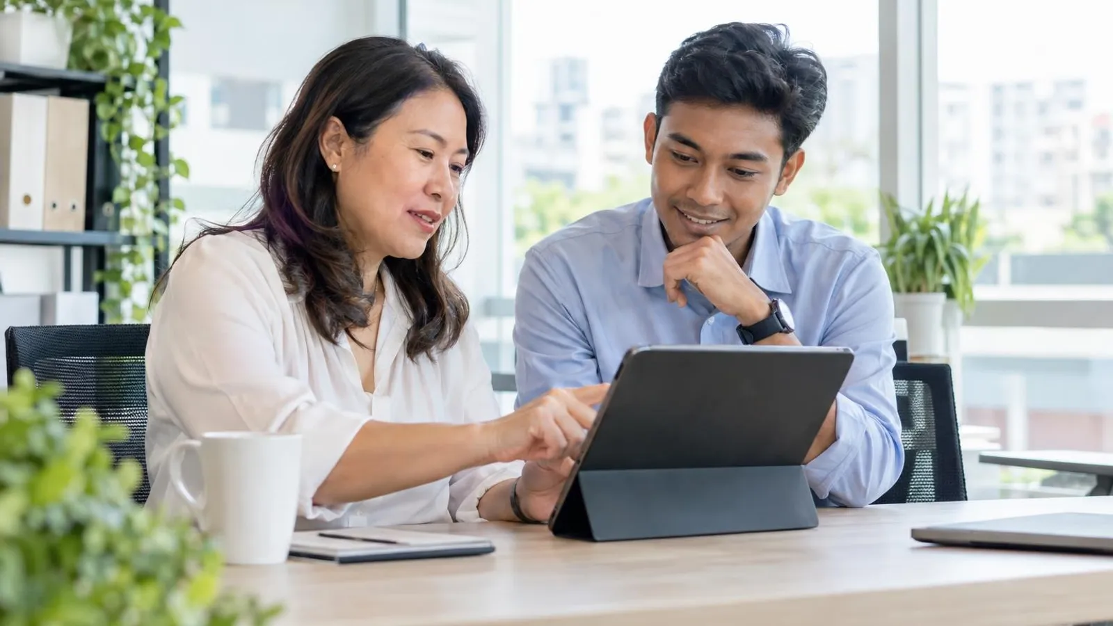 An HR manager and a staff member reviewing a leave calendar on a tablet at a bright office table