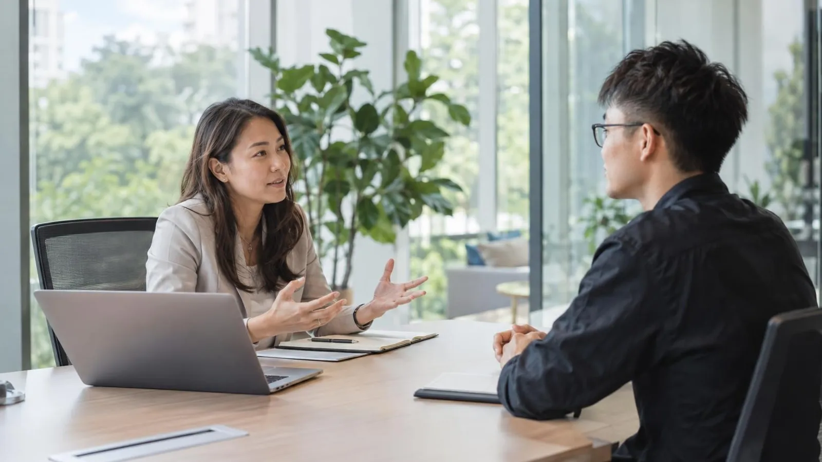 A recruiter interviewing a young software engineer across a bright modern meeting-room table