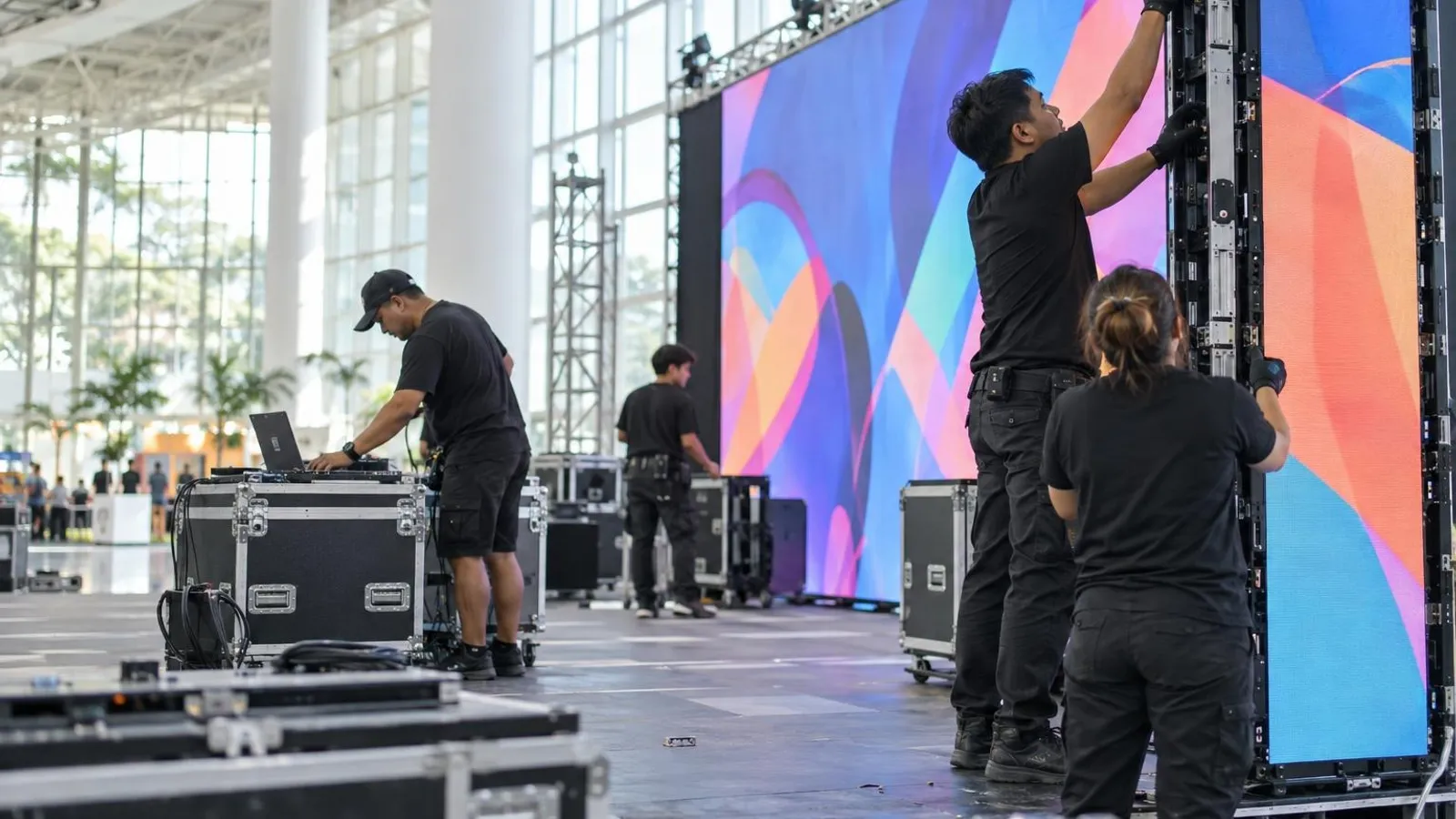 Technicians assembling a large LED video wall on an event stage in a bright exhibition hall
