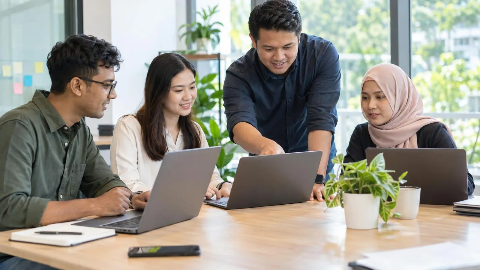 An IT consultant helping a small office team set up their laptops around a bright meeting table