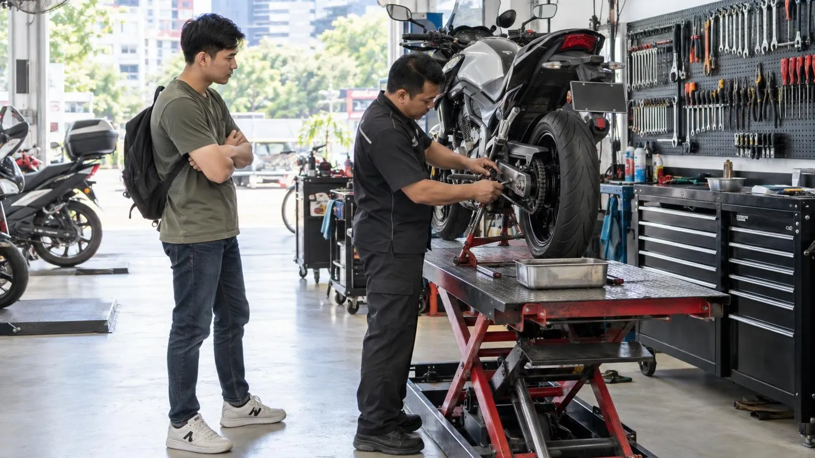 A mechanic servicing a motorcycle on a lift in a bright workshop while the rider watches