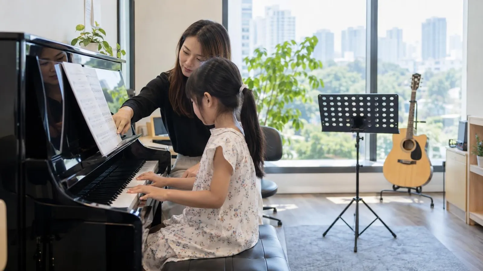 A music teacher guiding a child at a piano in a bright Singapore music school studio