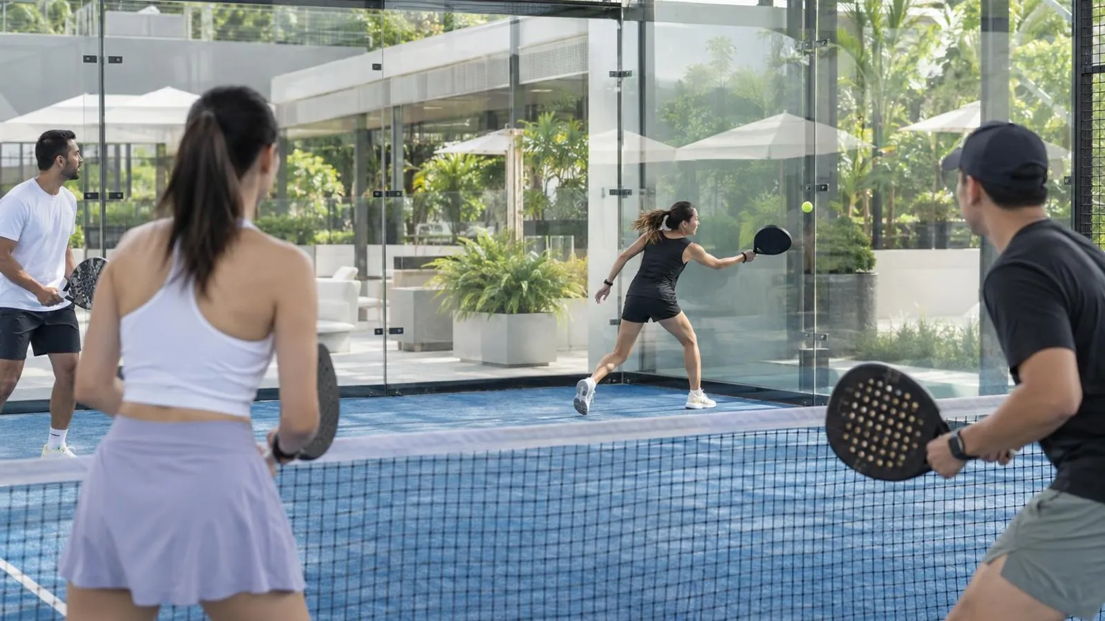 Friends playing padel on a glass-walled court in daylight