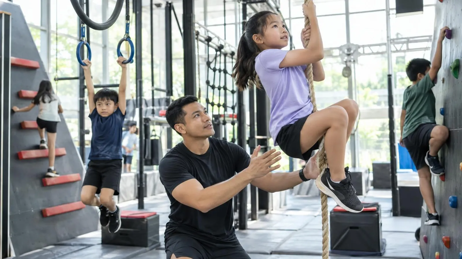 Children practising on a ninja obstacle course in an indoor gym with a coach