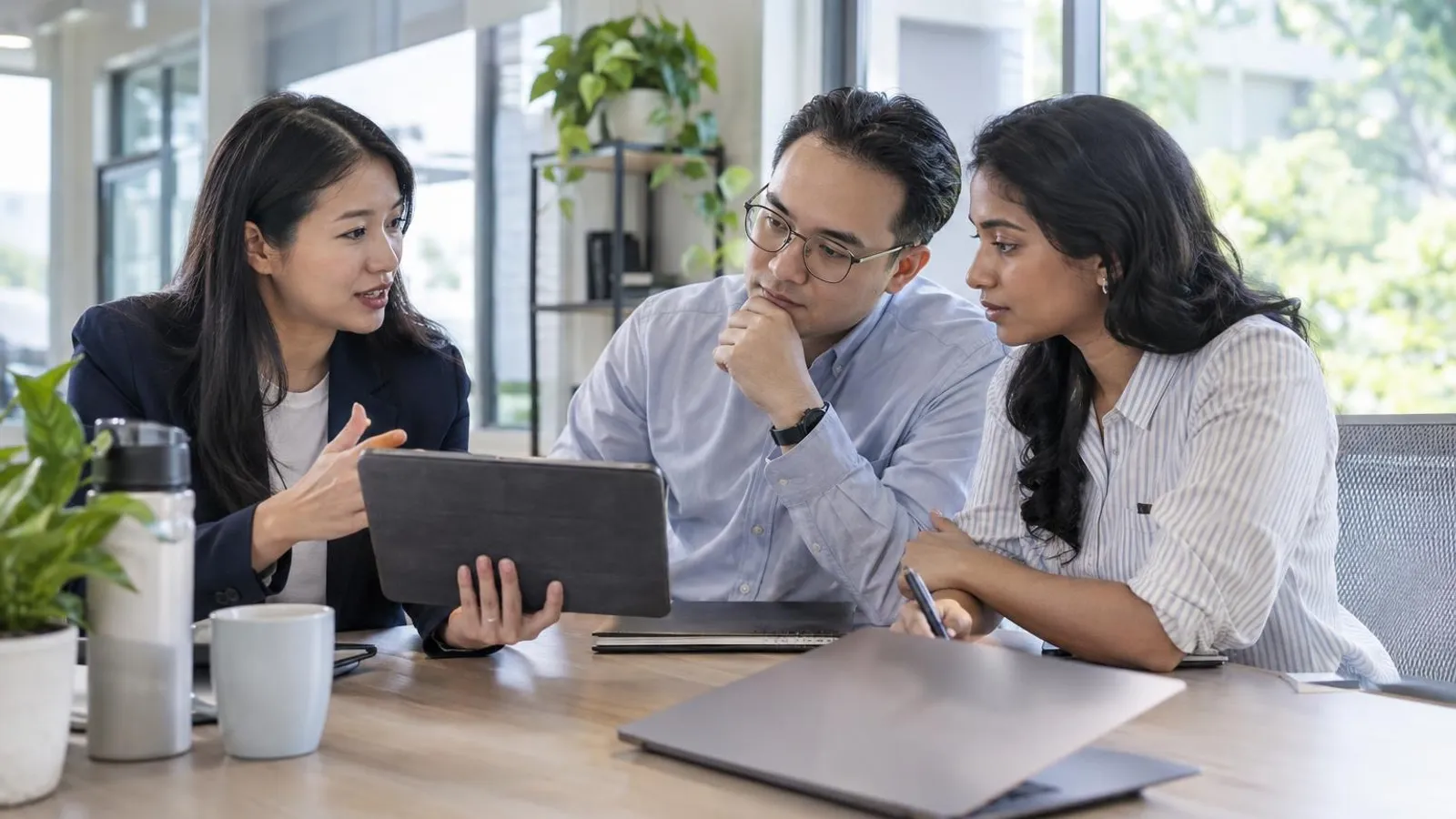 A consultant explaining a data-protection plan on a tablet to two office staff in a bright meeting room