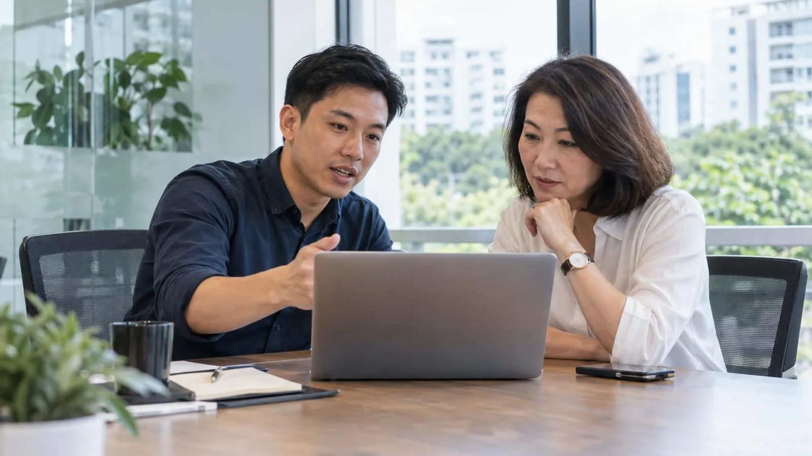 A security consultant reviewing a vulnerability report on a laptop with a client in a bright modern meeting room