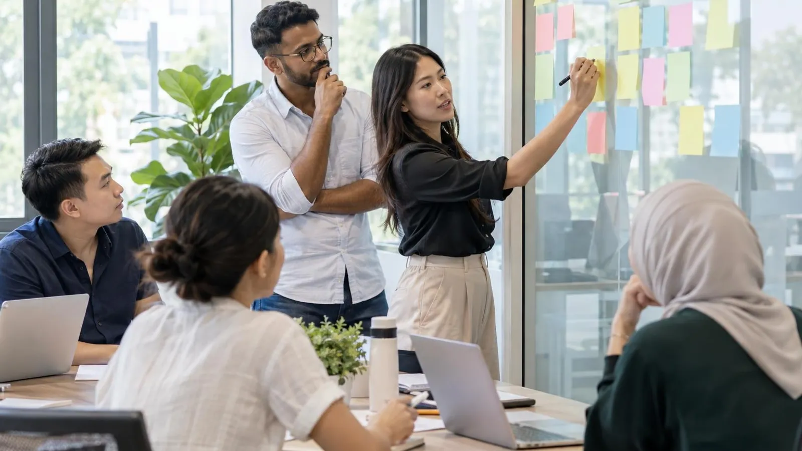 A trainer and learners planning with sticky notes on a glass wall in a bright training room