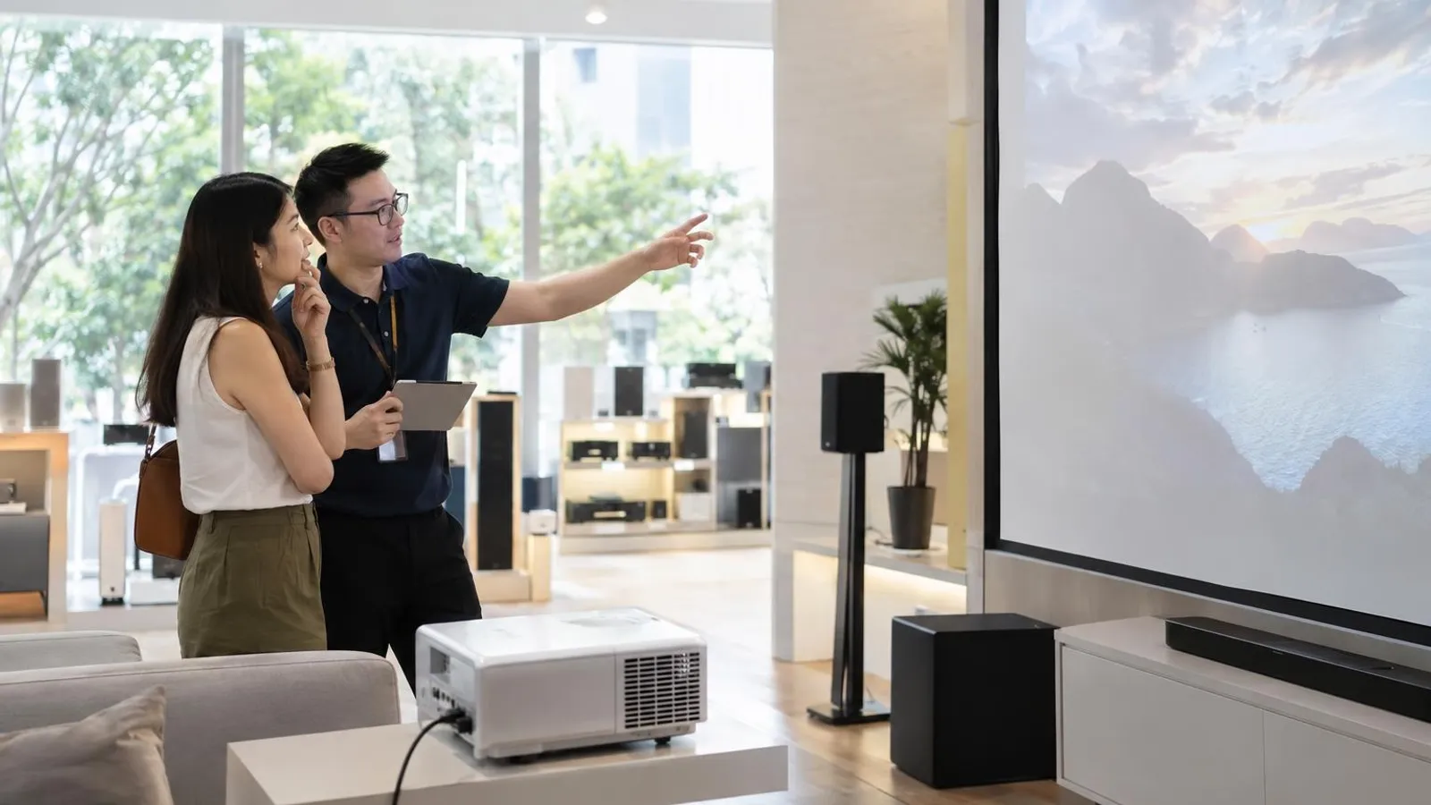 A customer and a shop assistant looking at a projector pointed at a screen in a bright demonstration room
