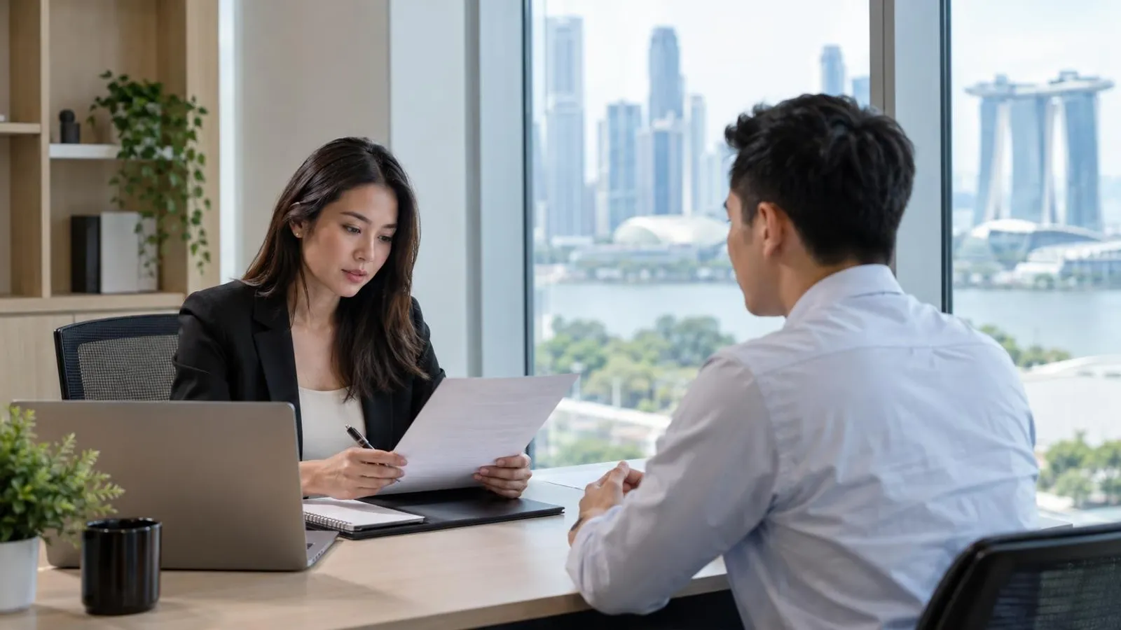 A recruiter reviewing a resume across a desk from a job candidate in a Singapore office